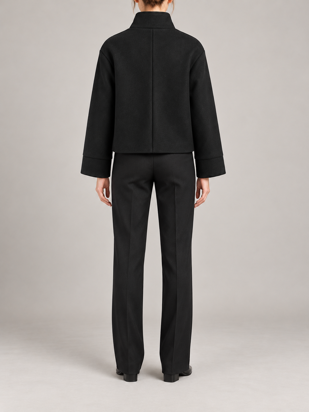 black short boxy high-neck coat with asymmetric button front and broad straight sleeves, back view on a model