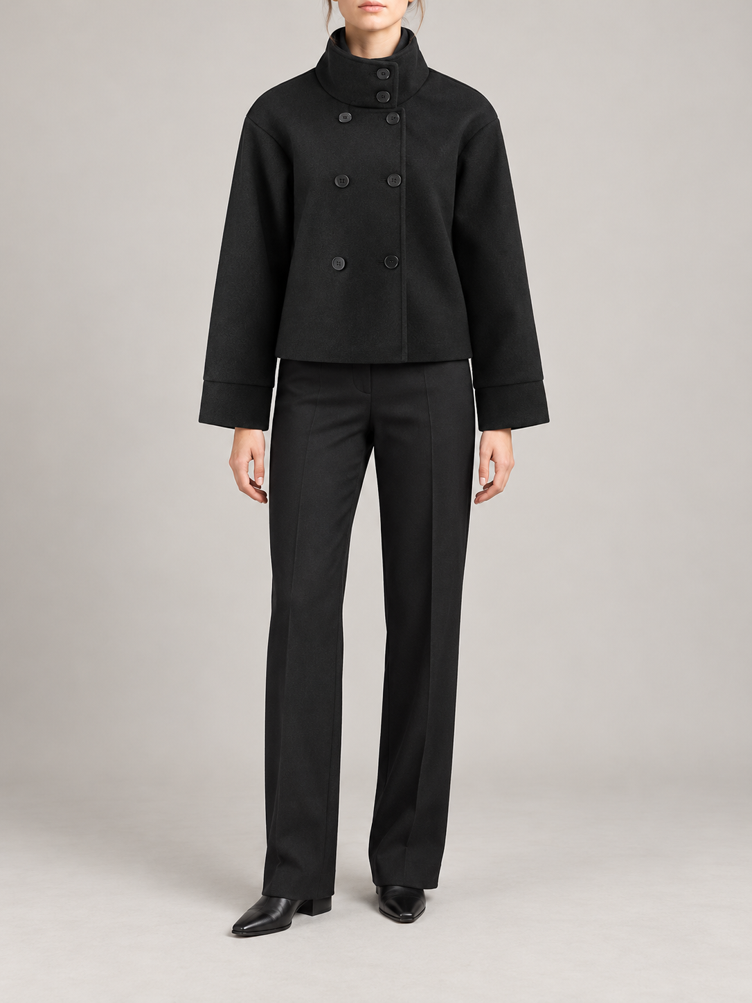black short boxy high-neck coat with asymmetric button front and broad straight sleeves, front view on a model