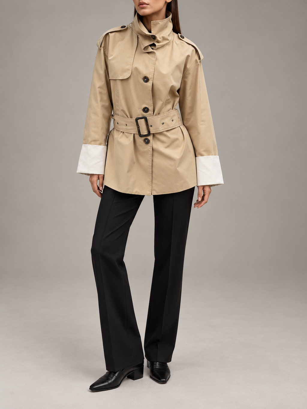 beige belted short trench with tall collar, dark buttons, shoulder tabs, chest storm flap and wide white contrast cuffs, front view on a model
